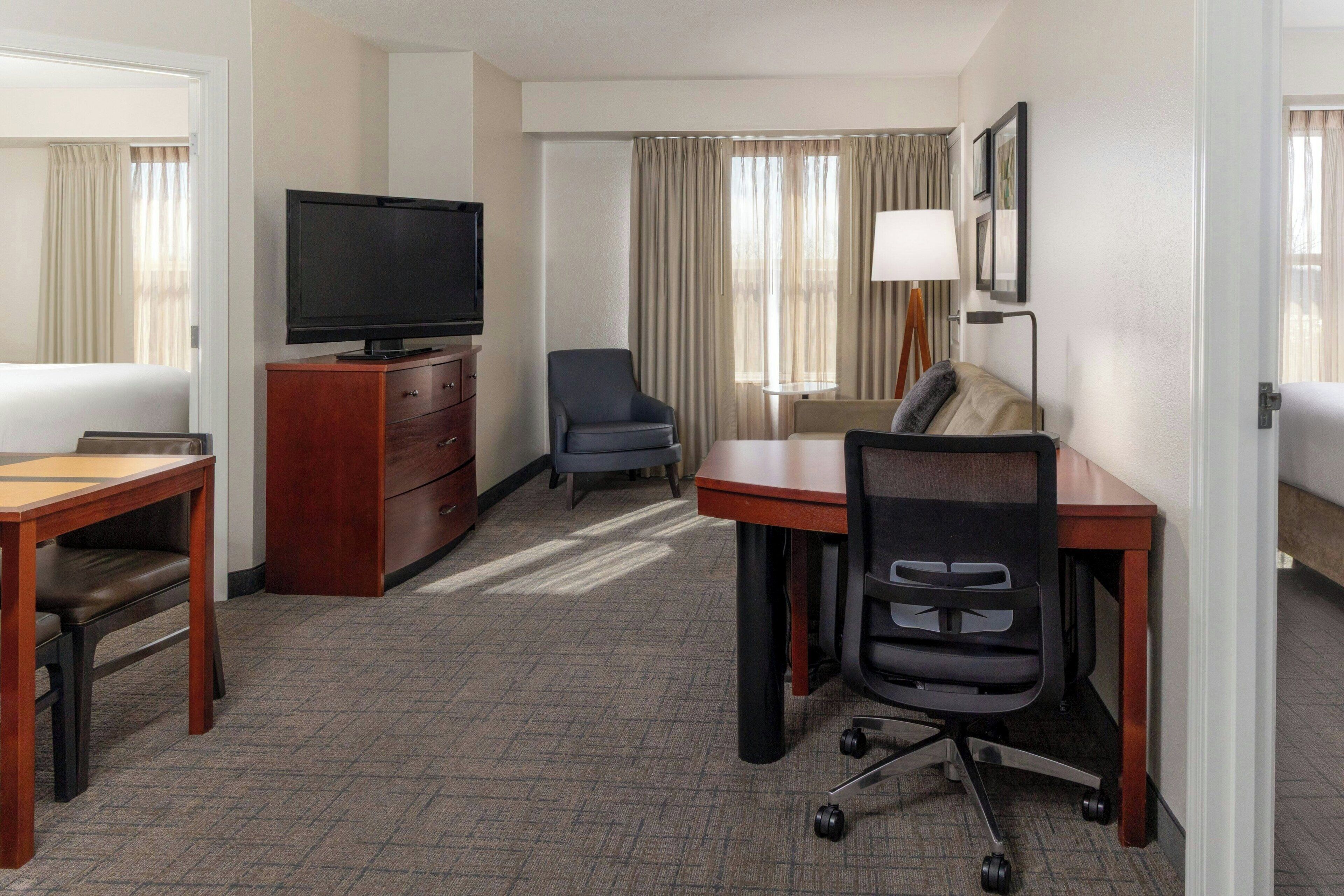 Ein Hotelzimmer mit Flachbildfernseher, Schreibtisch mit Stuhl, einer Couch, einer Lampe und einem Bett.