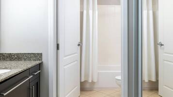 A bathroom with a granite countertop, a toilet, and a shower area with white curtains.