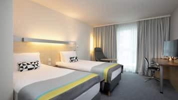 A hotel room with two beds, a desk, a chair, and a TV.