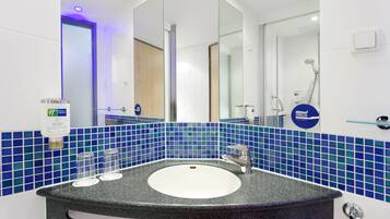 Une salle de bain moderne avec un lavabo rond, un grand miroir et des murs recouverts de carreaux bleus.