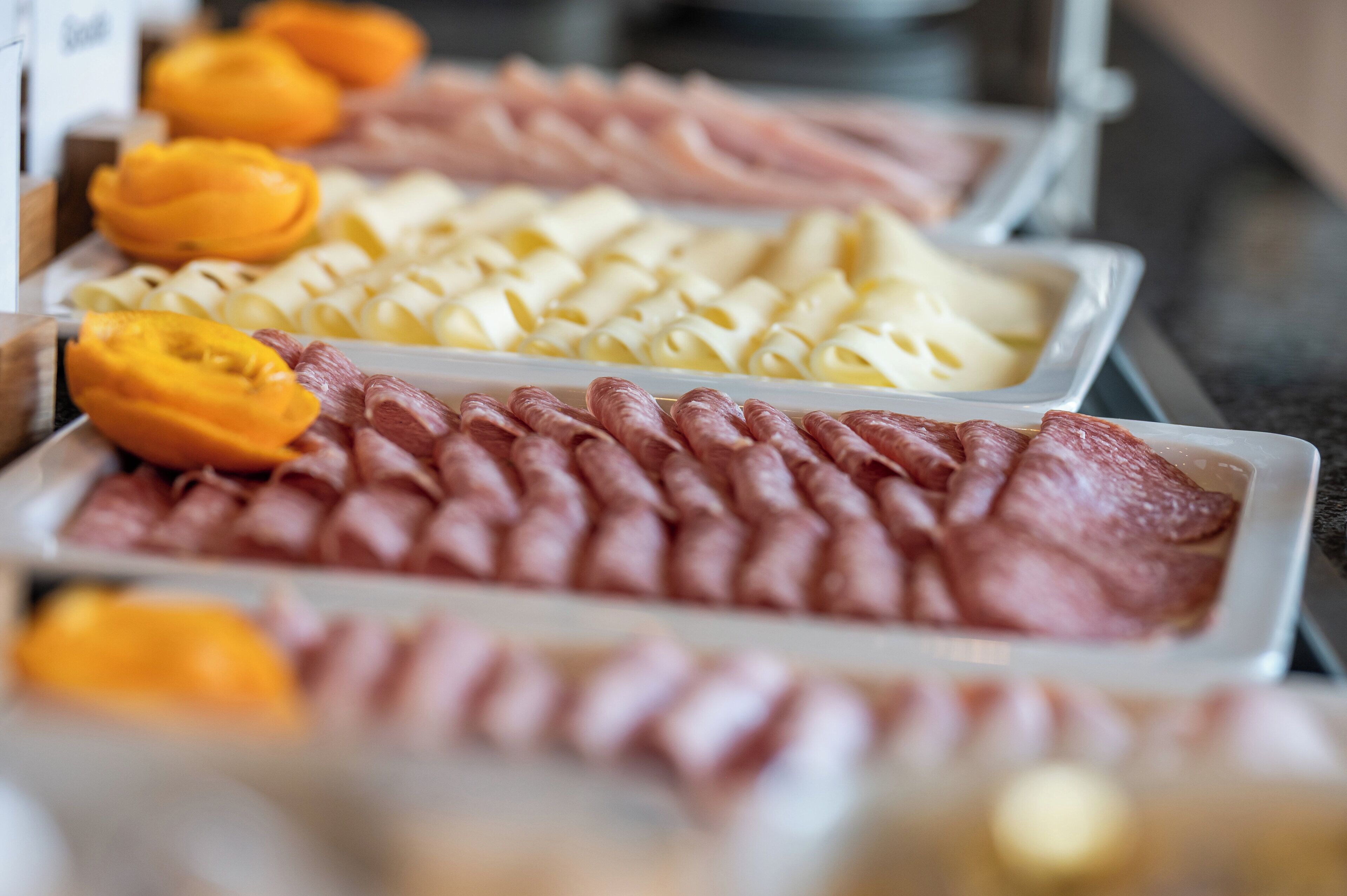 Un bufé con diversos alimentos, incluyendo carnes cortadas, quesos y frutas.