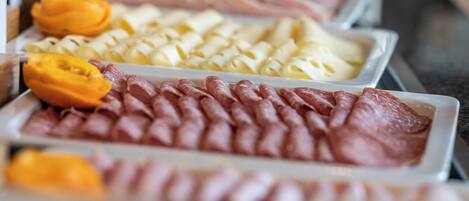 Un bufé con diversos alimentos, incluyendo carnes cortadas, quesos y frutas.