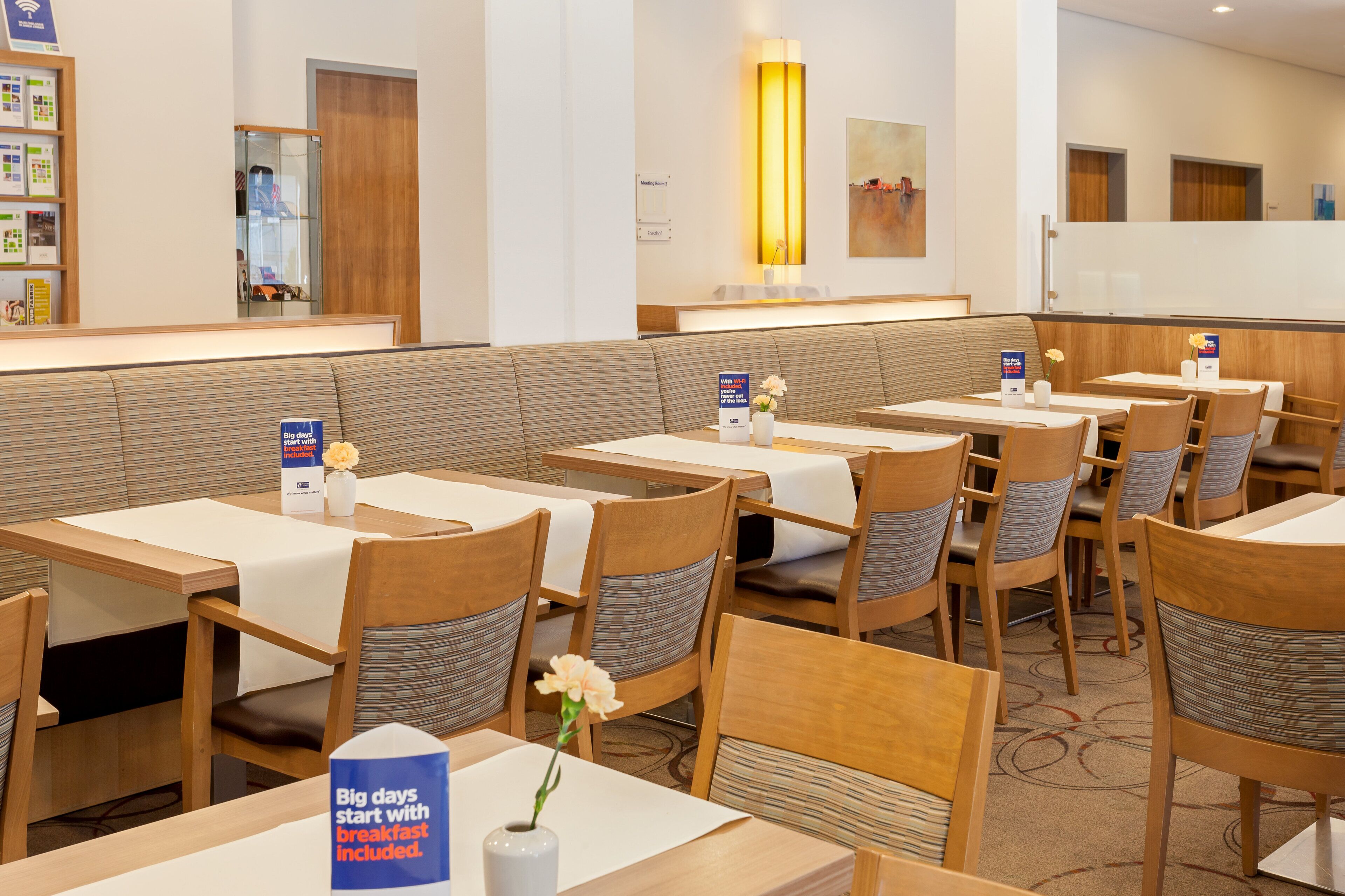 A hotel dining area with tables and chairs, a reception desk, and a wall-mounted lamp.