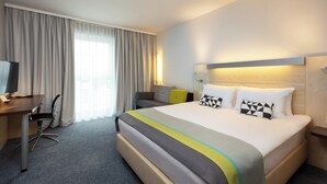 A hotel room with a bed, a desk, a chair, a TV, and a window with curtains. - Holiday Inn Express Nuernberg-Schwabach by IHG (Schwabach)