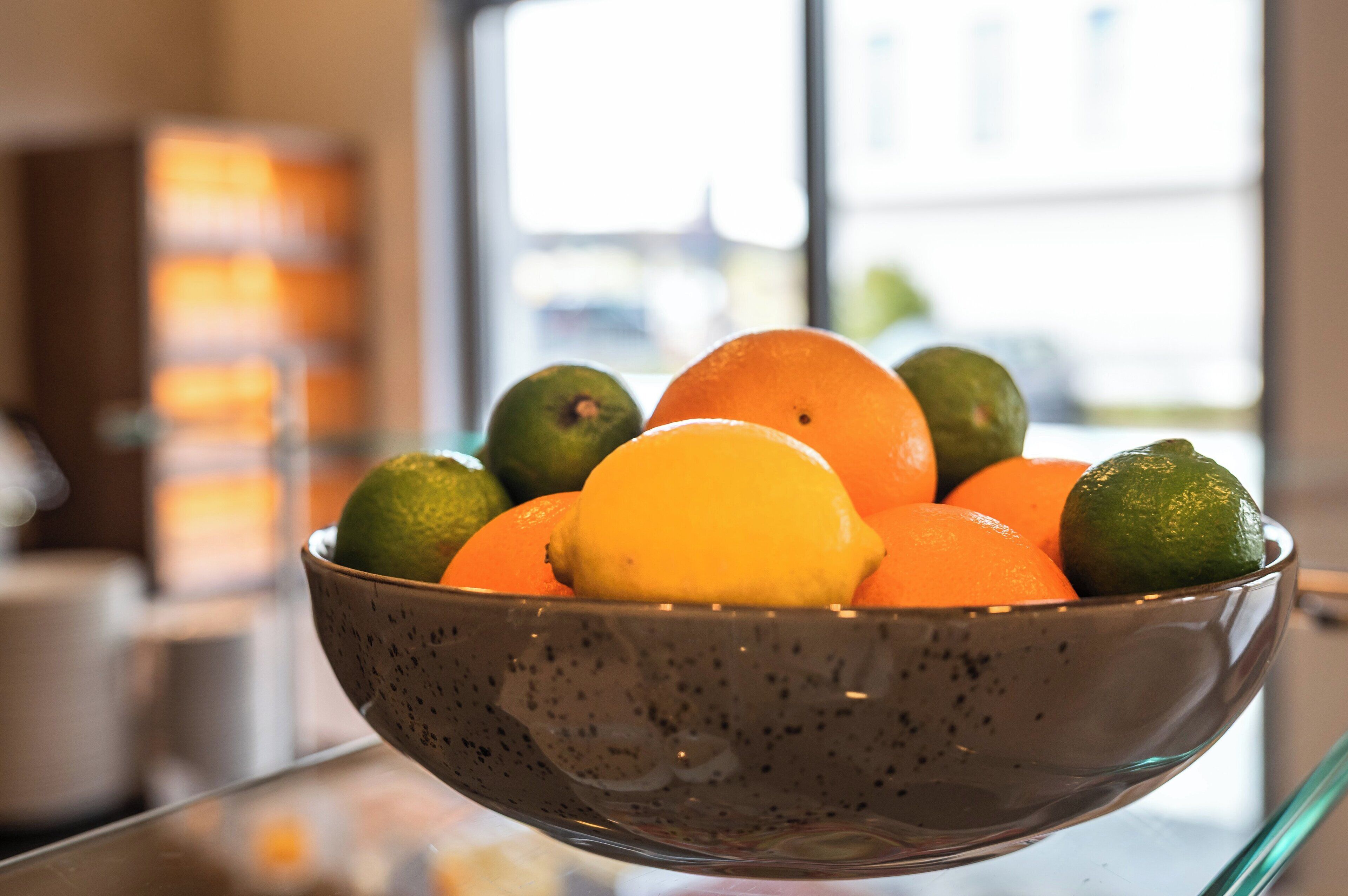 Un saladier rempli de fruits, notamment des oranges et des citrons verts.