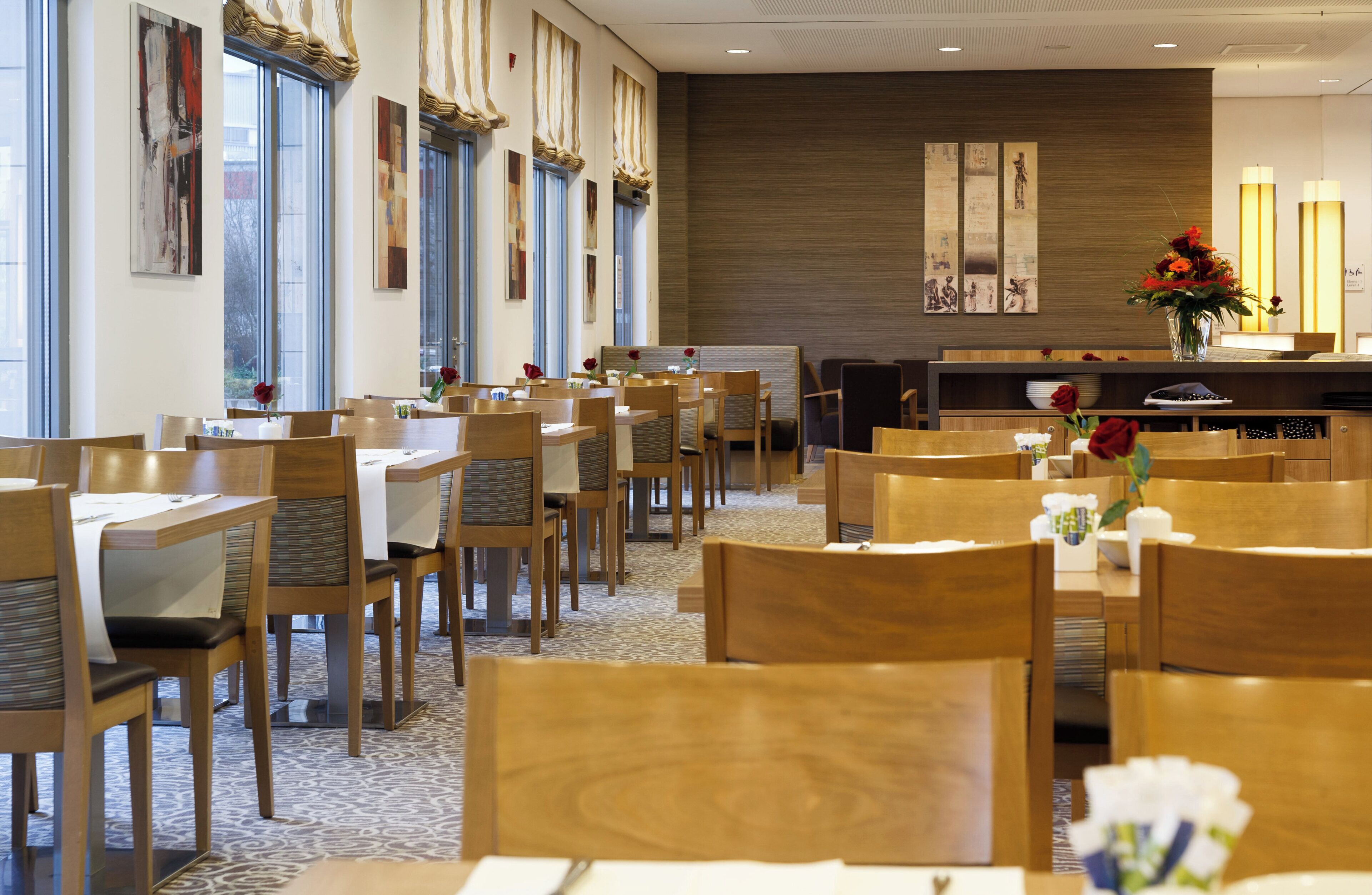 A hotel dining area with multiple tables and chairs, a reception desk, and artwork on the walls.