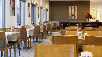 A hotel dining area with multiple tables and chairs, a reception desk, and artwork on the walls.