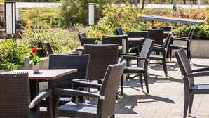 An outdoor seating area with wicker chairs and tables, surrounded by greenery and a pathway. - Holiday Inn Express Nuernberg-Schwabach by IHG (Schwabach)