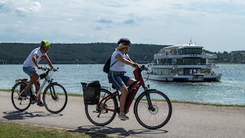 Deux cyclistes sur une piste cyclable, au bord d’un lac, avec un bateau en arrière-plan.