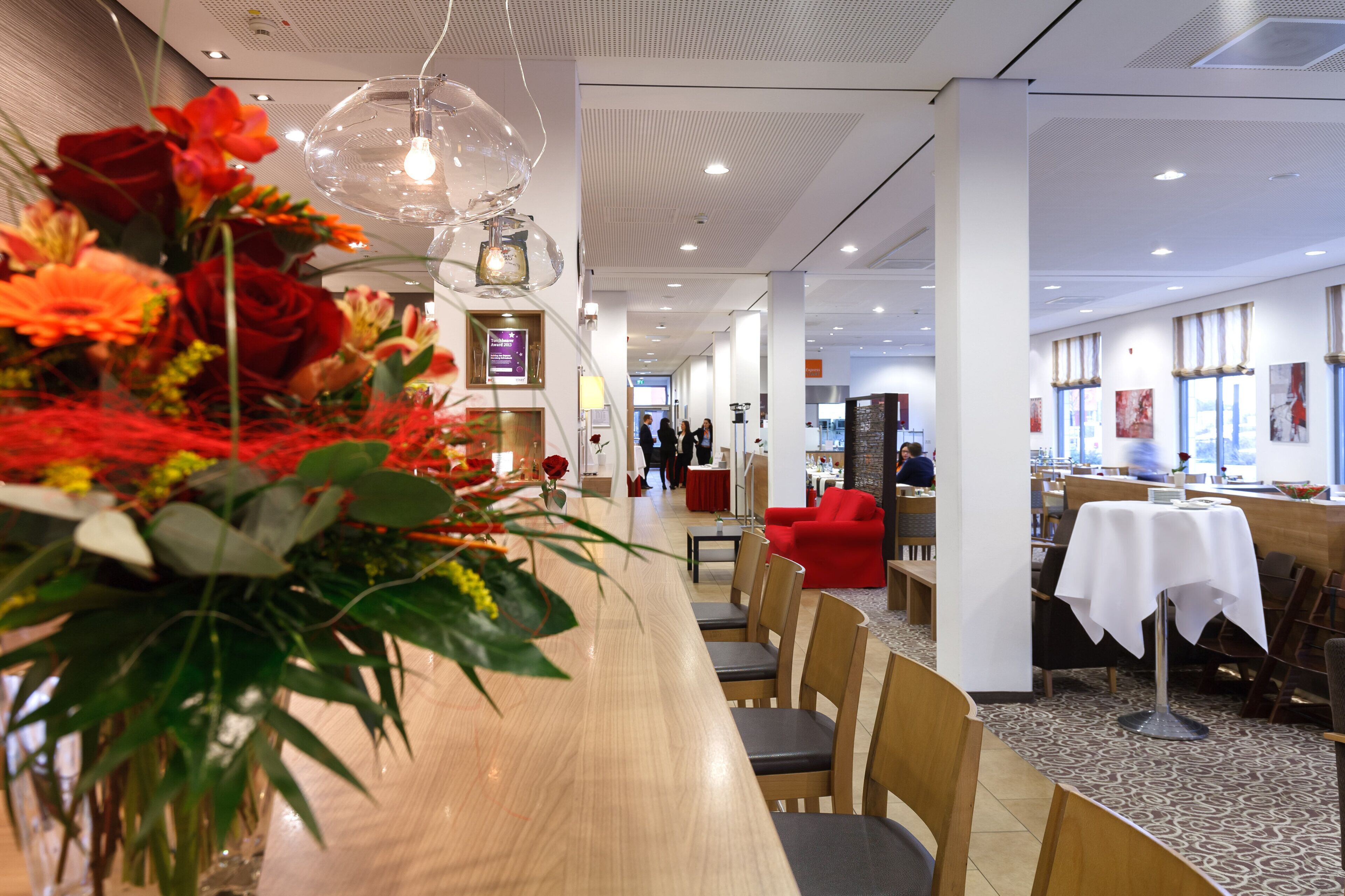 A restaurant with a long wooden counter, red chairs, and a floral centerpiece.