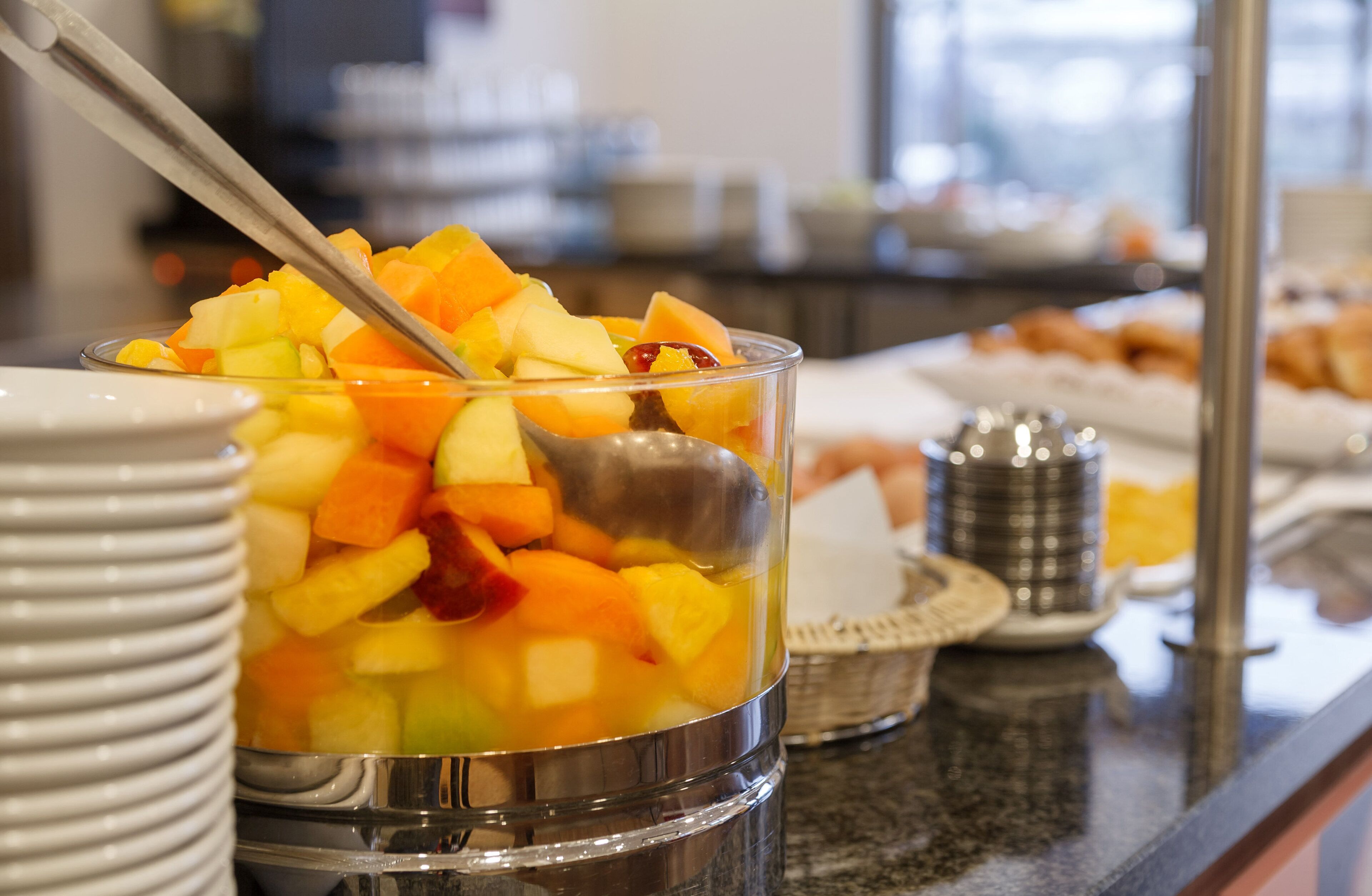 Buffet com diversas frutas e uma tigela de metal com uma colher.