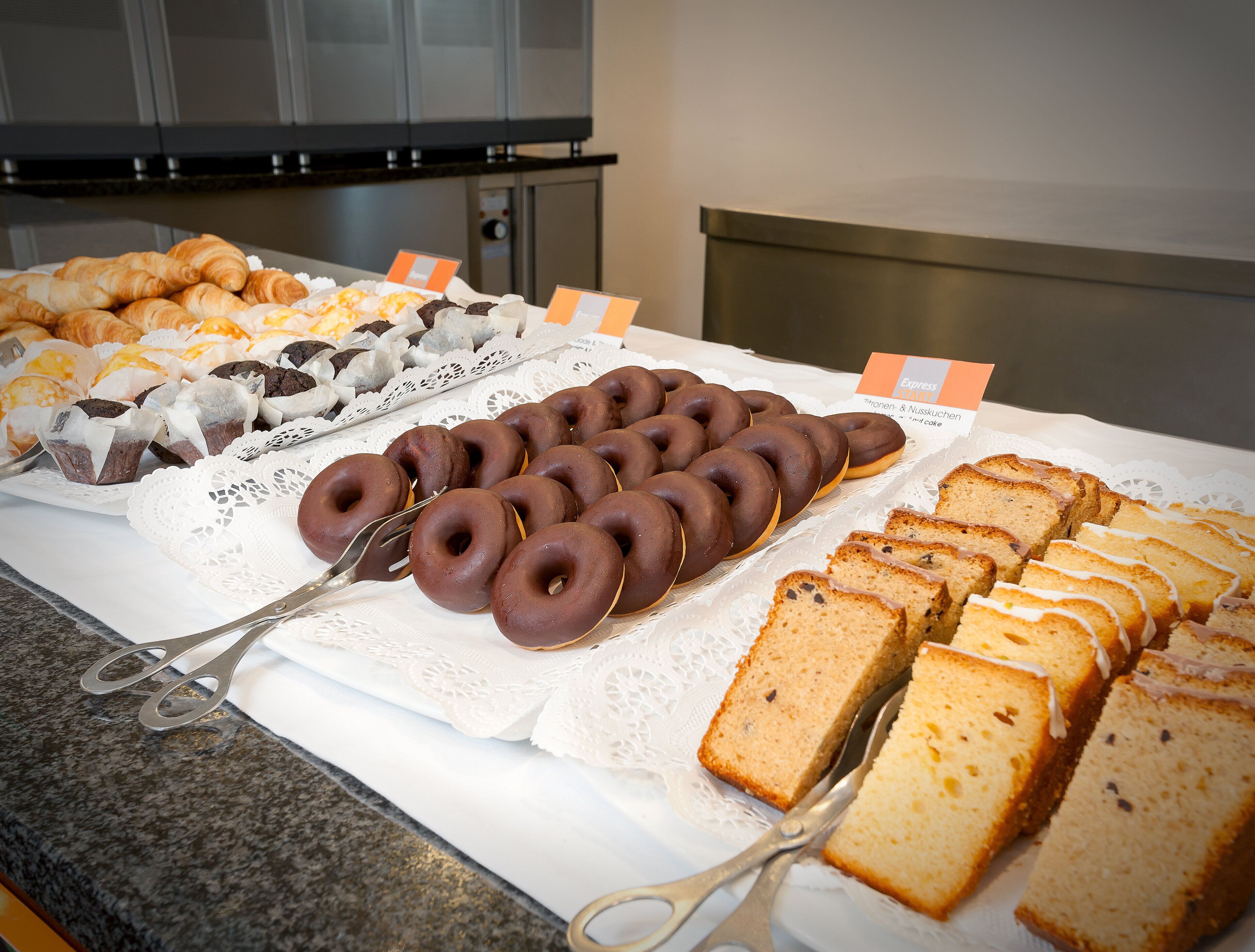 A buffet table with various baked goods including pastries, donuts, and cake slices.