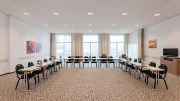Une salle de conférence avec une longue table, des chaises et un téléviseur posé sur un meuble.