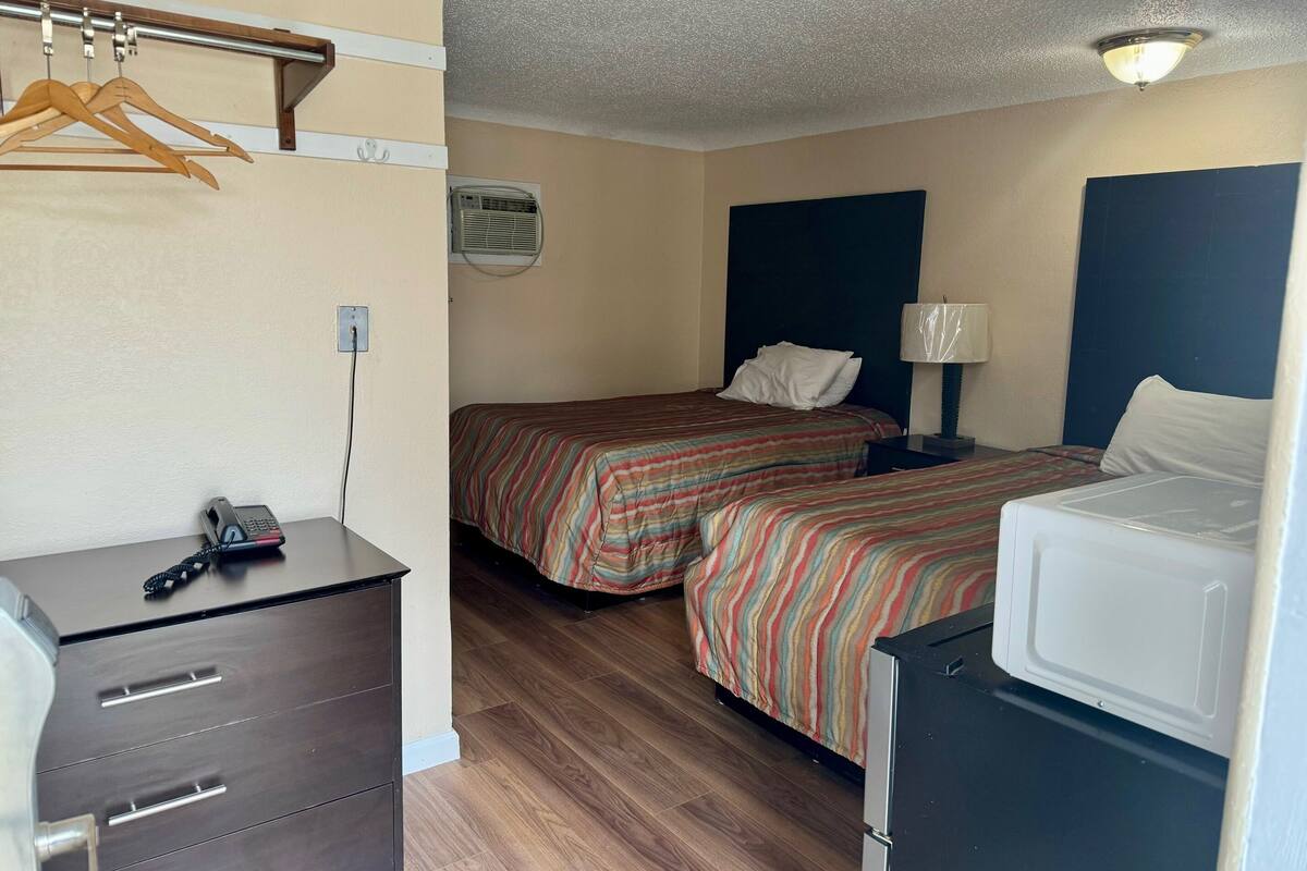 A hotel room with two beds, a small desk, a washing machine, and a ceiling fan.