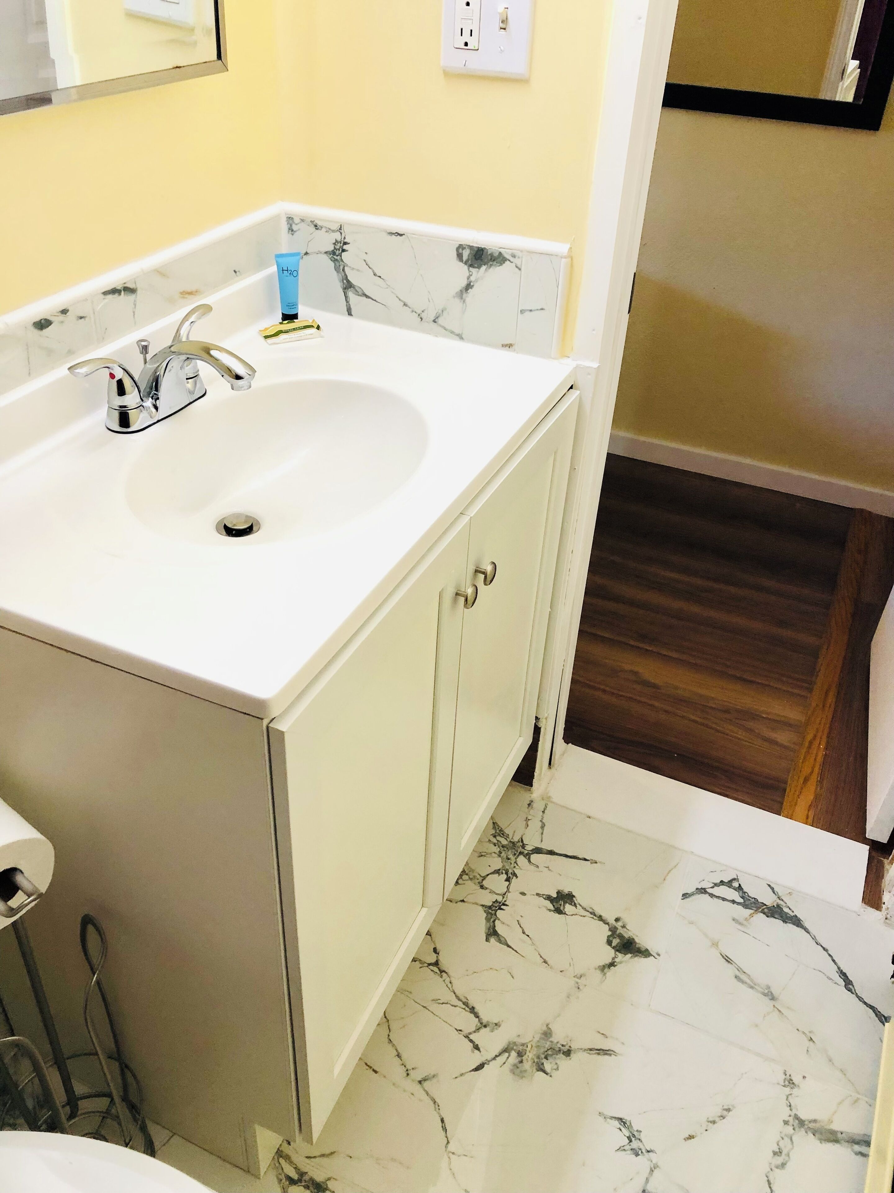 A bathroom with a white sink, chrome faucet, and a marble-patterned floor.
