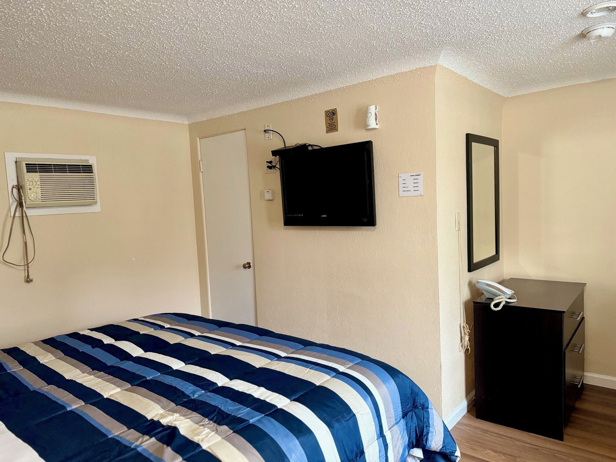 A hotel room with a bed, a TV, a phone, and a small desk.