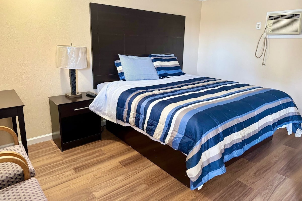 A hotel room with a bed, a nightstand, a lamp, and a wooden floor.