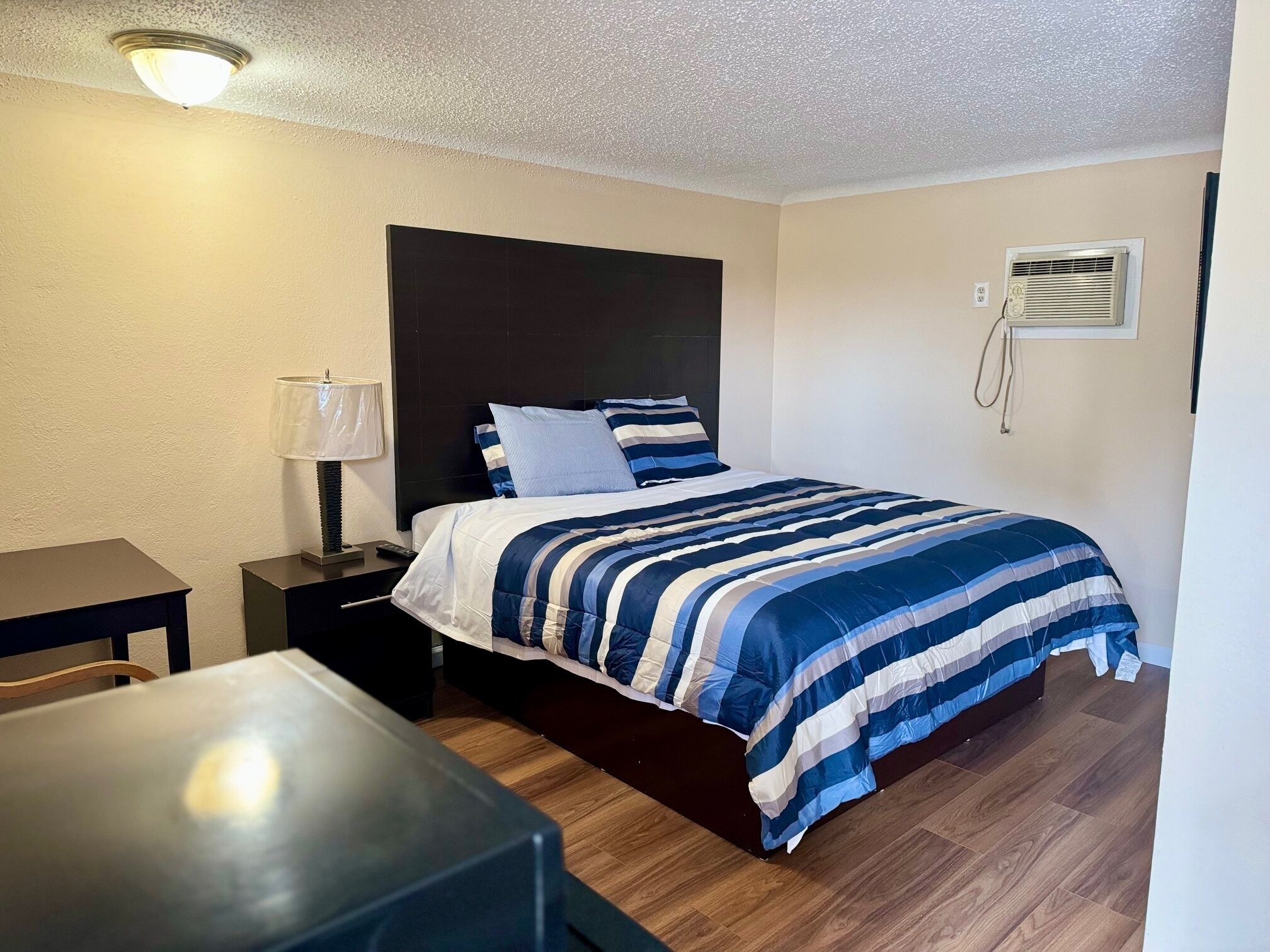 Quarto de hotel bem arrumado, com cama, mesa de cabeceira, abajur e uma pequena mesa.