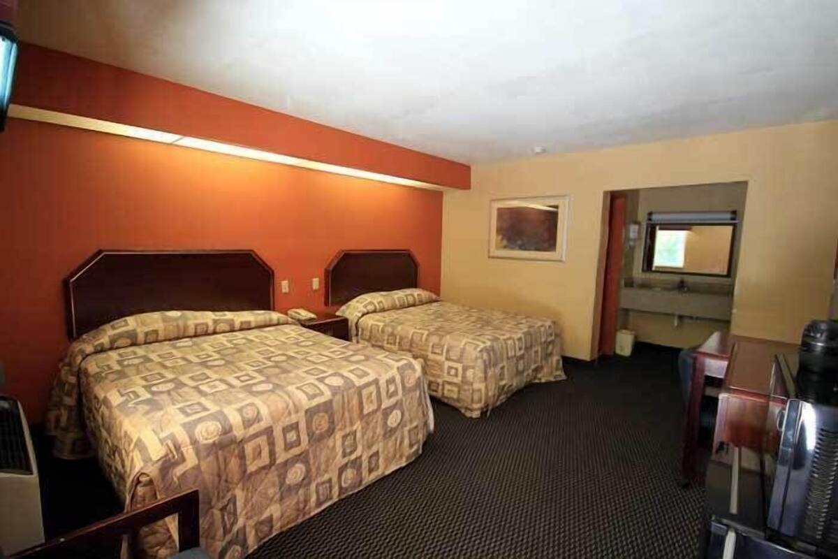 Una habitación de hotel con dos camas, un escritorio, una silla, un televisor y una ventana.