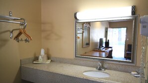 Une salle de bain dotée d’un plan de toilette en granit, d’un lavabo, d’un miroir, d’un porte-serviettes et d’un sèche-cheveux.