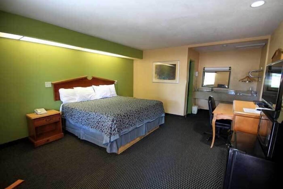 Habitación de hotel con una cama, un escritorio, una silla, un espejo y un televisor.