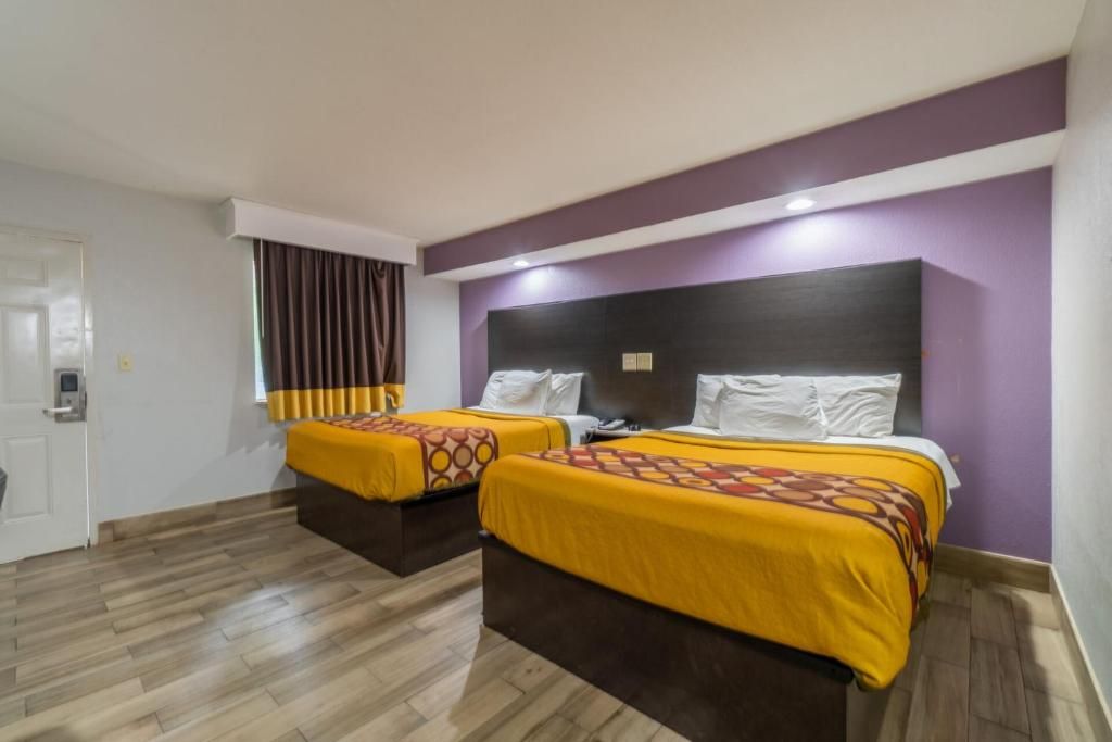A hotel room with two beds, a wooden floor, and purple walls.