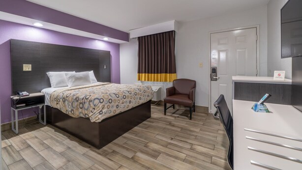 Une chambre d’hôtel avec un lit, un bureau, une chaise, une table de chevet et une porte.