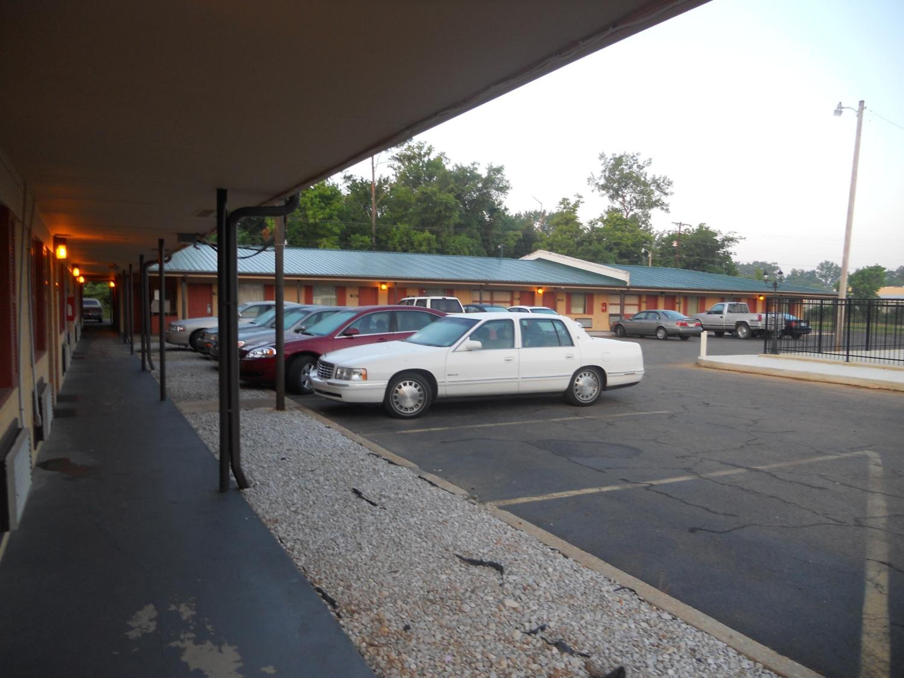 A motel with a covered parking area, multiple cars parked, and a building with a green roof.