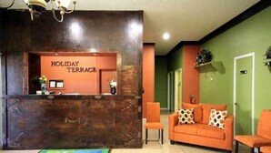 Un espace d’accueil doté d’un comptoir de réception en bois portant l’inscription « Holiday Terrace », d’un mur végétal et d’un canapé orange agrémenté de coussins à motifs.