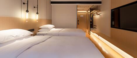 Una habitación de hotel moderna con dos camas, cabecero de madera, televisor montado en la pared e iluminación colgante.
