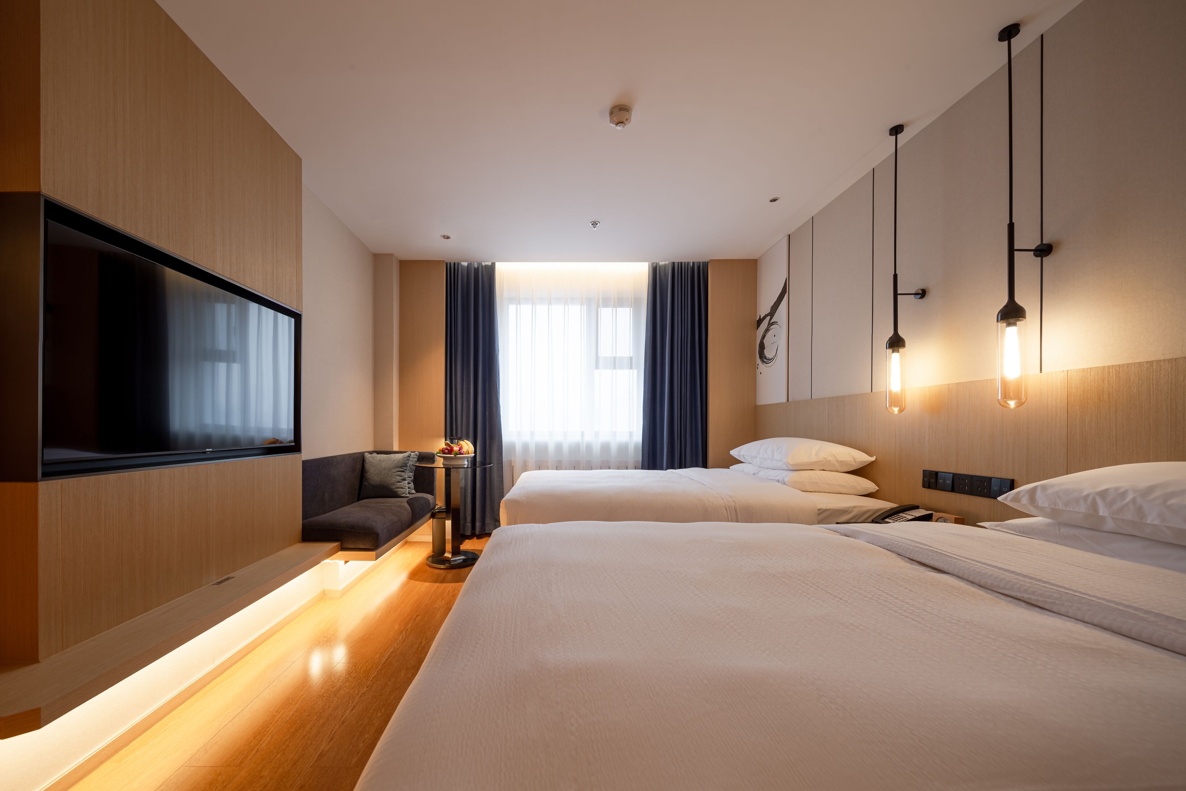 Een hotelkamer met twee bedden, een flatscreen televisie, een bank en een nachtkastje met lamp.