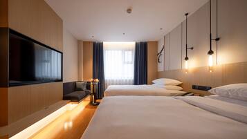 A hotel room with two beds, a flat-screen TV, a sofa, and a bedside table with a lamp.
