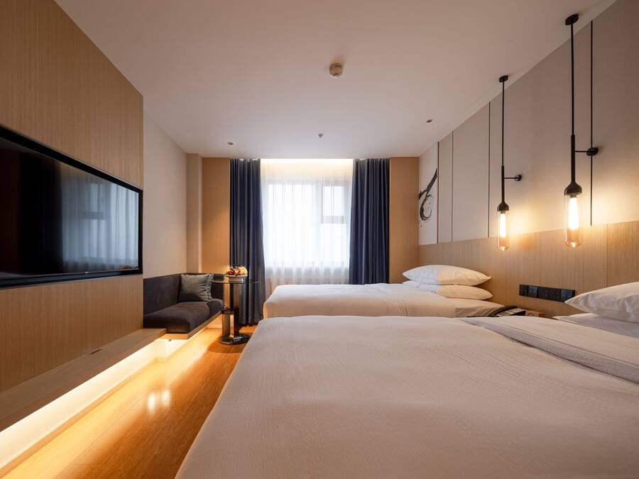 A hotel room with two beds, a flat-screen TV, a sofa, and a bedside table with a lamp.