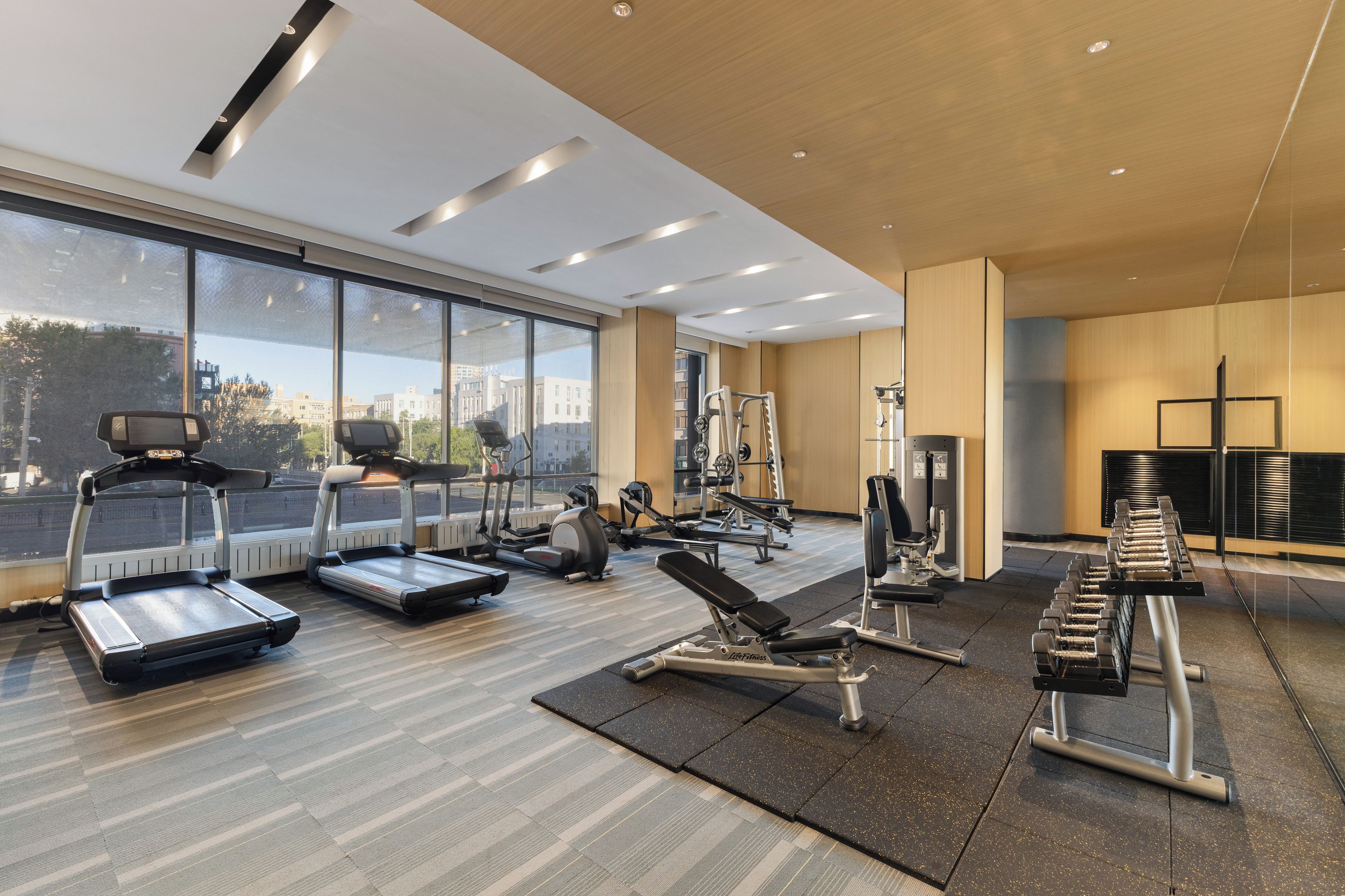 Un gimnasio moderno con cintas de correr, máquinas de pesas y un amplio ventanal con vistas a la ciudad.