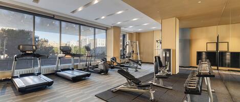 Un gimnasio moderno con cintas de correr, máquinas de pesas y un amplio ventanal con vistas a la ciudad.