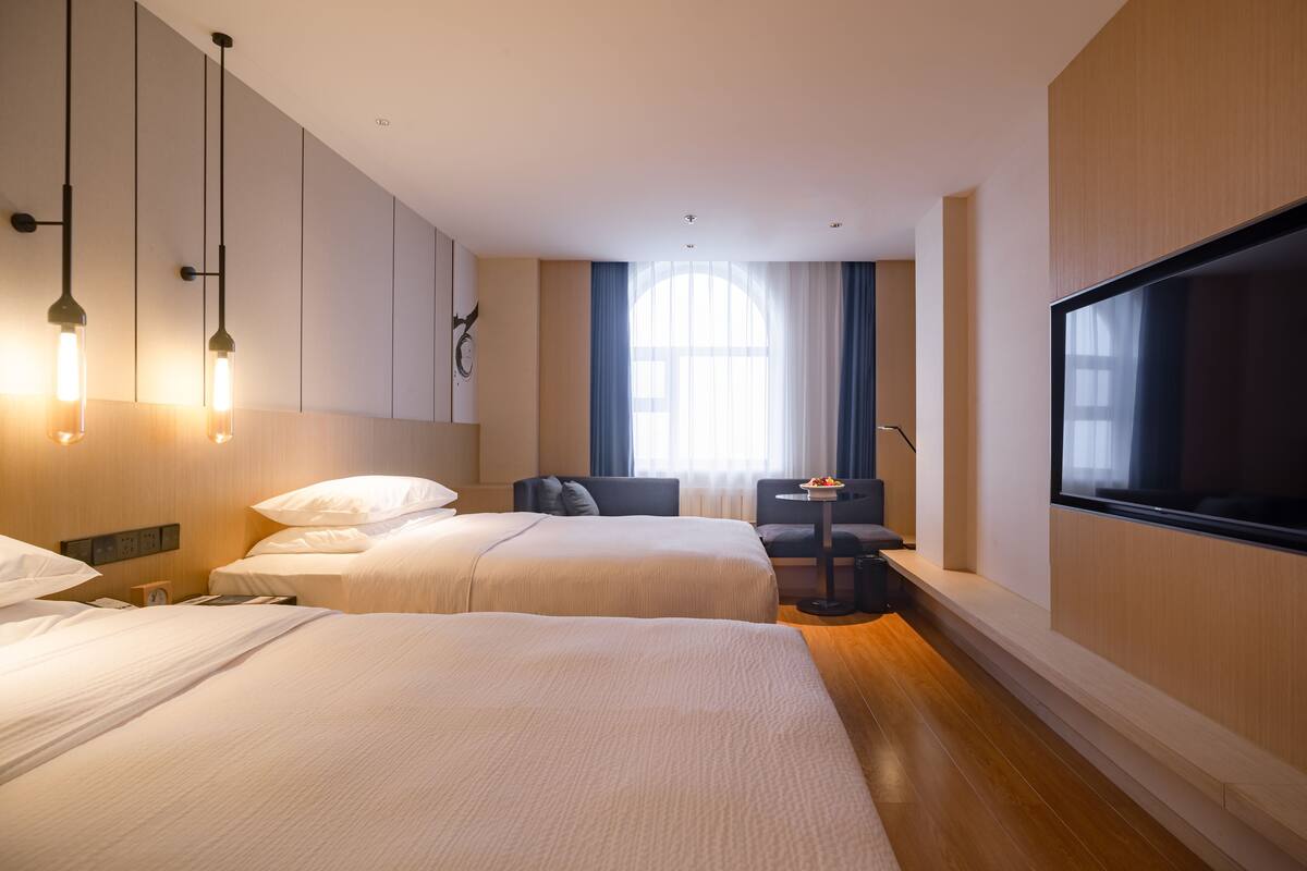 A hotel room with two beds, a TV, a small table, and a window with curtains.