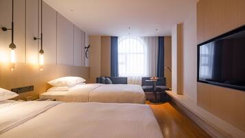 A hotel room with two beds, a TV, a small table, and a window with curtains.