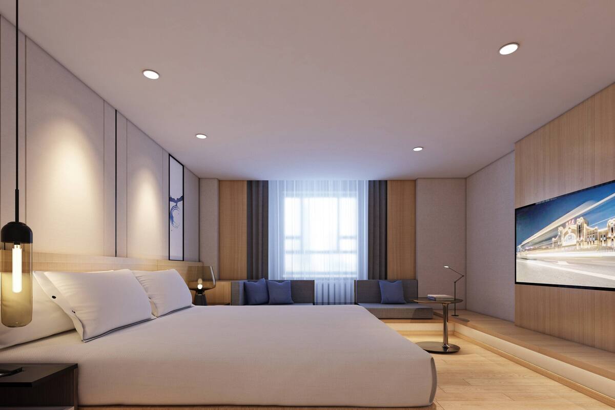 A modern hotel room with a large bed, a seating area, a television, and a large window.