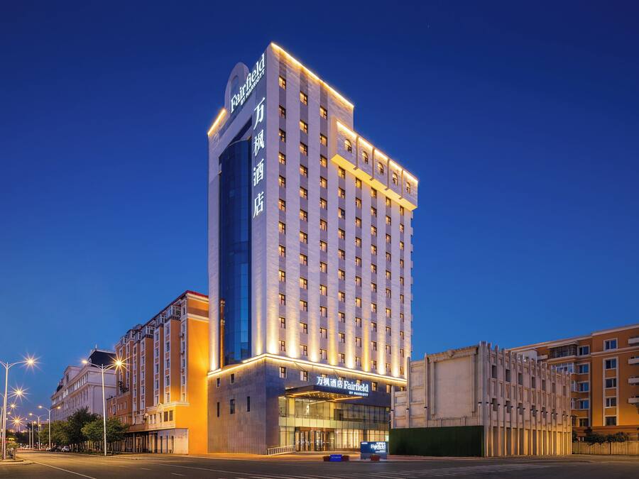 Un hotel de varios pisos con un cartel llamativo en la parte superior, una entrada amplia con puertas de vidrio y un diseño arquitectónico moderno.