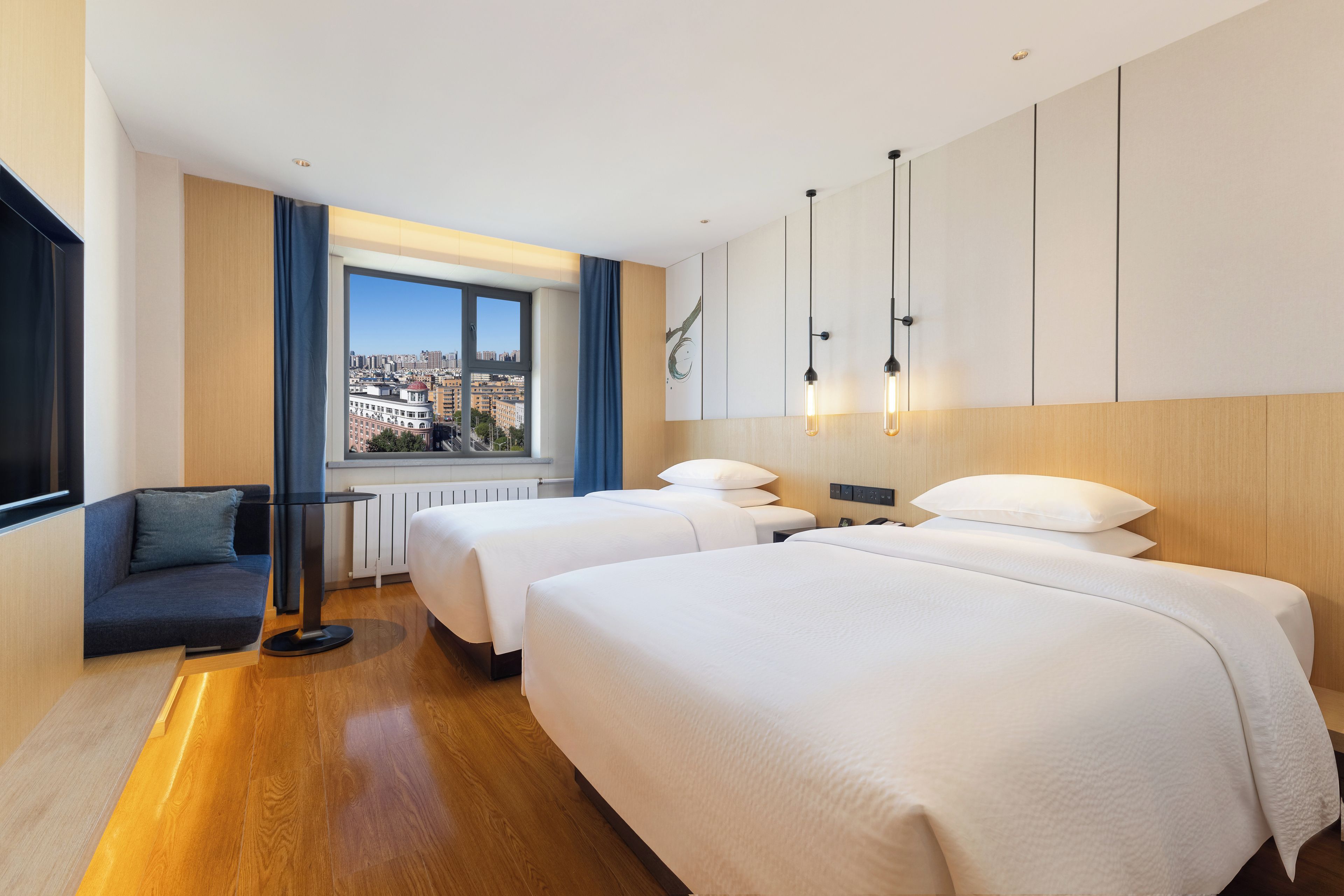 A hotel room with two beds, a sofa, a view of the city, and a modern design.