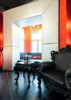 Um quarto com sofá de couro preto, mesa preta ornamentada e um lustre.