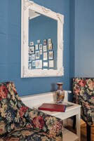 Een kamer met blauwe muren, een spiegel met witte lijst, meubels met bloemenprint en een decoratieve vaas op een witte tafel.