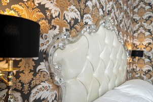 Um close-up de uma cama com cabeceira estofada branca e estrutura de metal ornamentada.