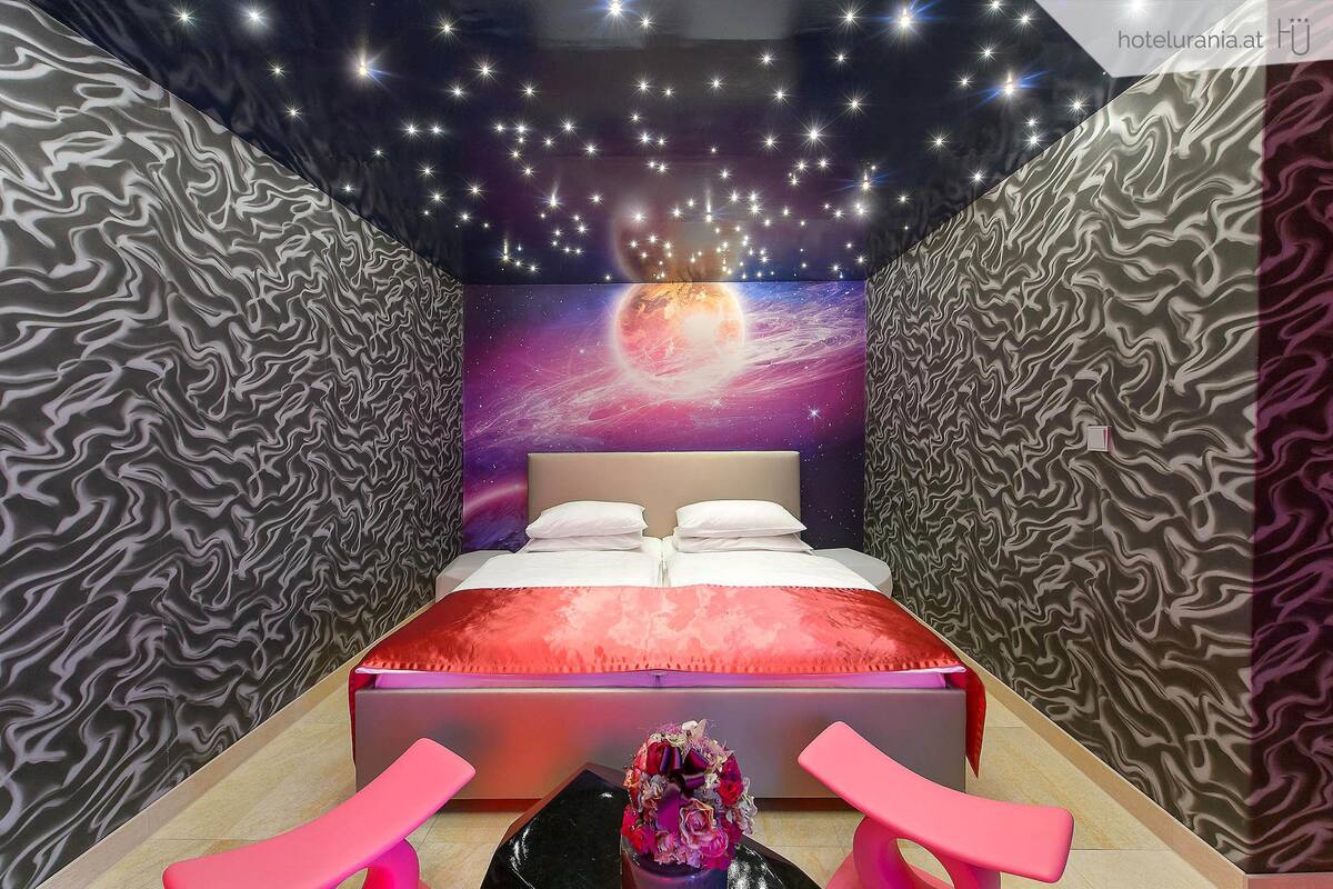 A modern bedroom with a bed, a starry ceiling, and a galaxy-themed wall.