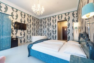 A bedroom with a large bed, a television mounted on the wall, a chandelier, and a mirror with a lamp.
