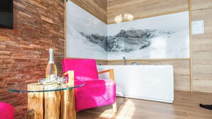 Um interior moderno com parede de madeira, uma grande obra de arte de montanhas emoldurada, uma cadeira rosa vibrante e uma mesa de vidro com uma garrafa.