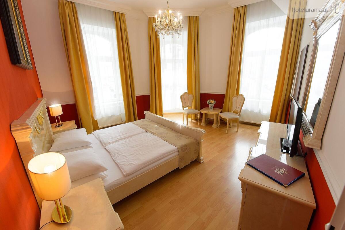 A hotel room with a bed, bedside table, lamp, chair, and a desk with a laptop.