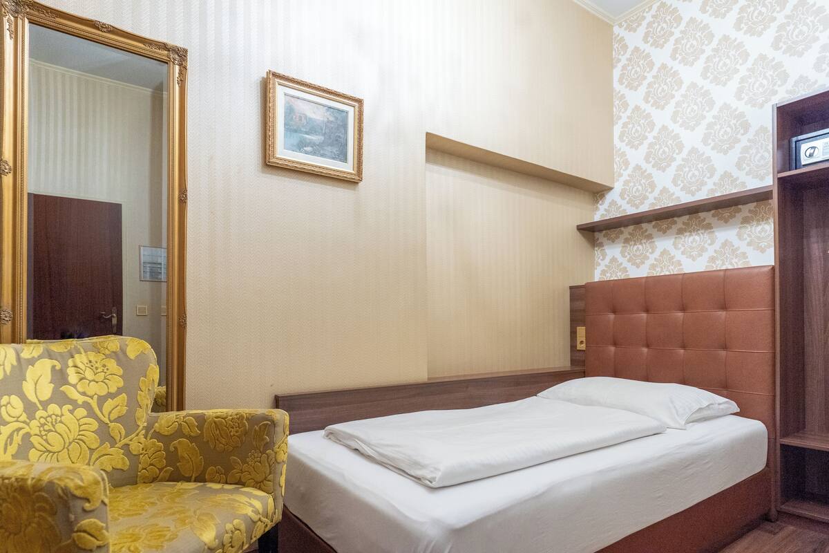 A hotel room with a bed, a chair, a mirror, a framed picture, and a patterned wall.