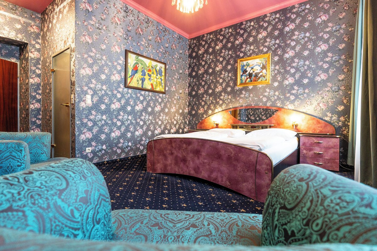Une chambre à coucher avec un papier peint à motifs floraux, un lit avec une tête de lit et une table de chevet.