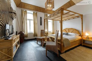 Un letto a baldacchino con testiera in legno, un tavolino rotondo con una candela, due poltrone in vimini, un comodino in legno con una lampada e un vaso grande su un comò.
